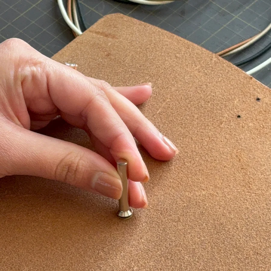A hand pressing an eyelet setting tool into a tan leather cover