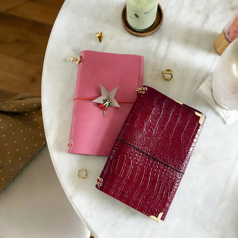 A finished pink leather journal and a red croc leather journal on a marble table